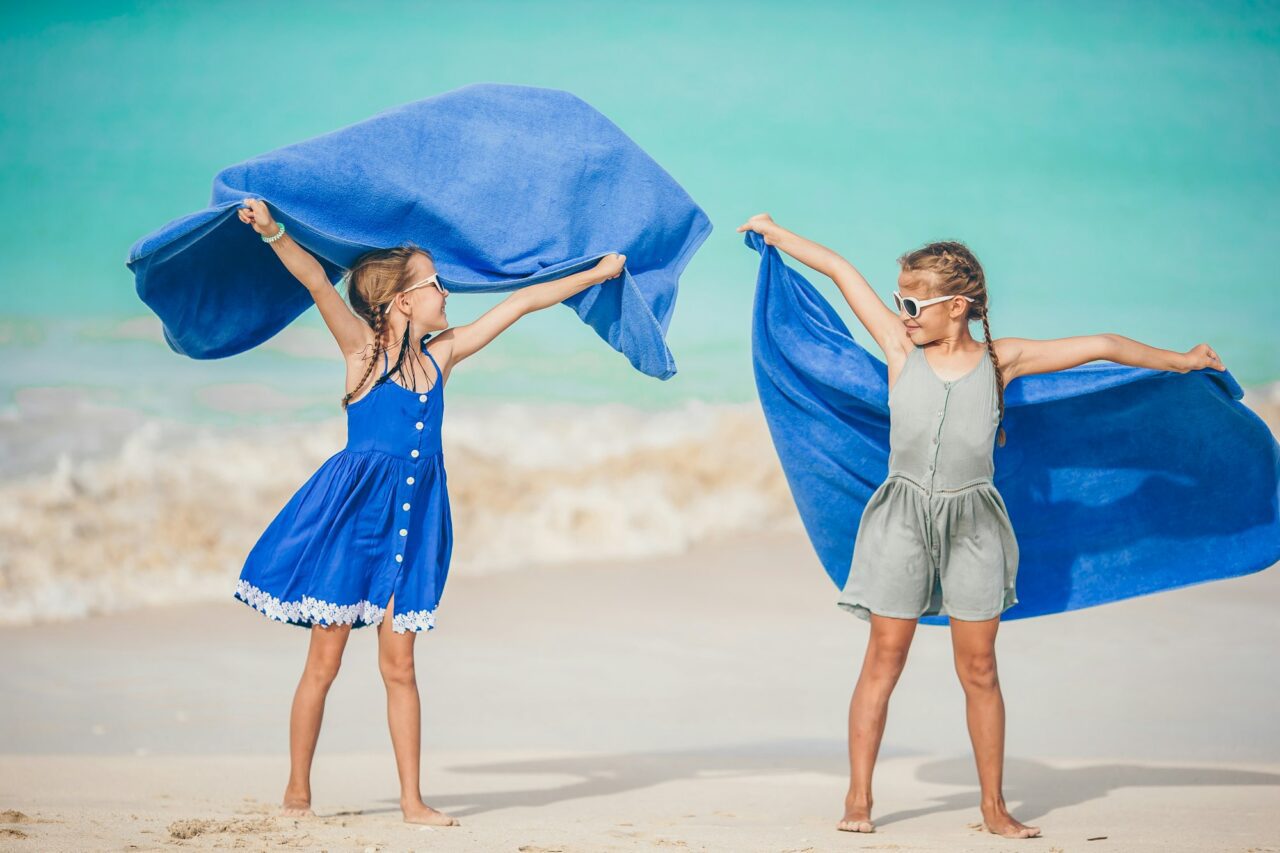 Little girls have fun with beach towel during tropical vacation