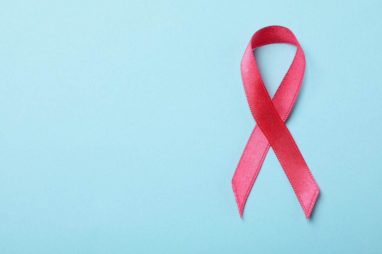 Pink awareness ribbon on blue background, space for text