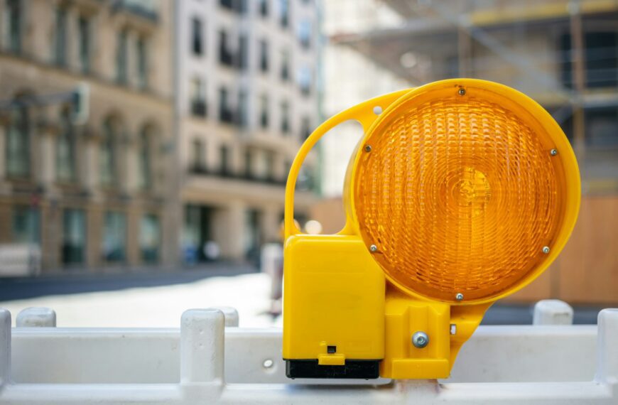Road construction concept. Orange reflector caution light. Blur city background, space.