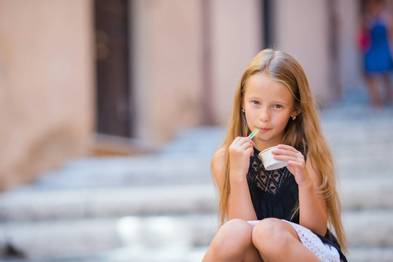 Adorable girl eating ice-cream outdoors at summer in the city