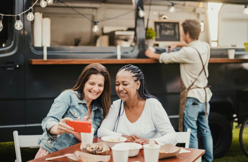 Adult women taking selfie at table near food truck