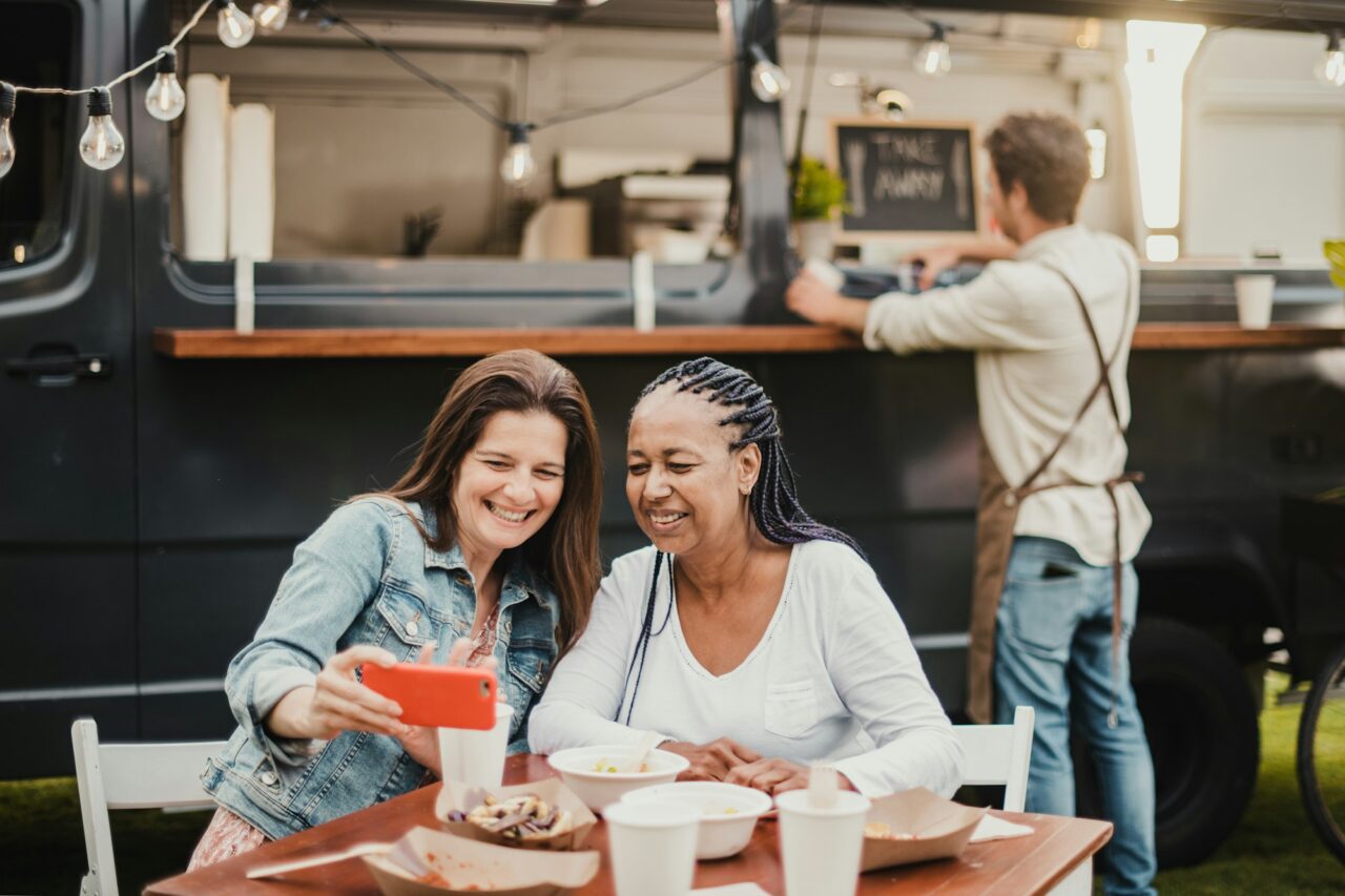 Adult women taking selfie at table near food truck