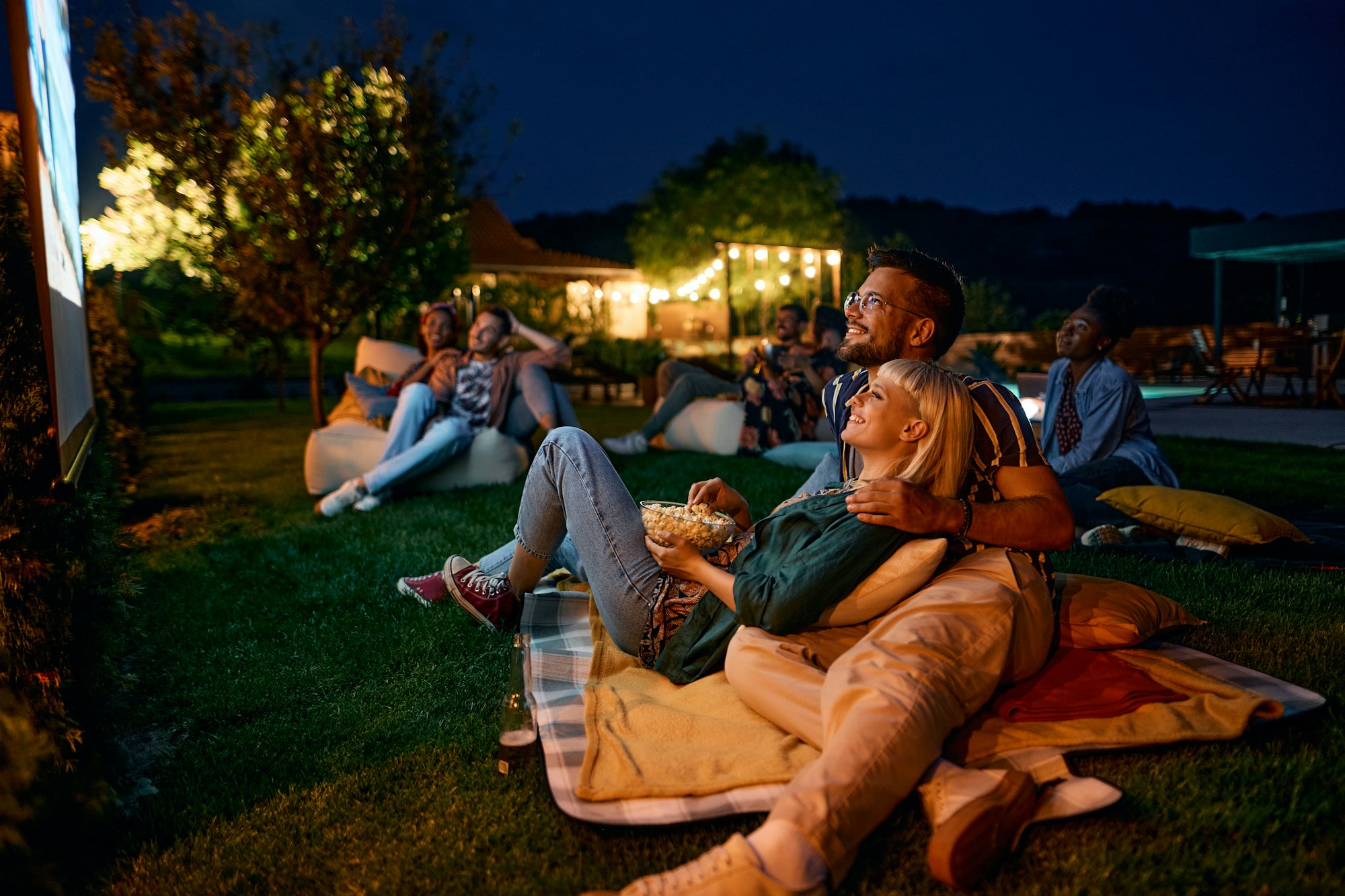 Happy couple enjoying in movie night with friends in the backyard.