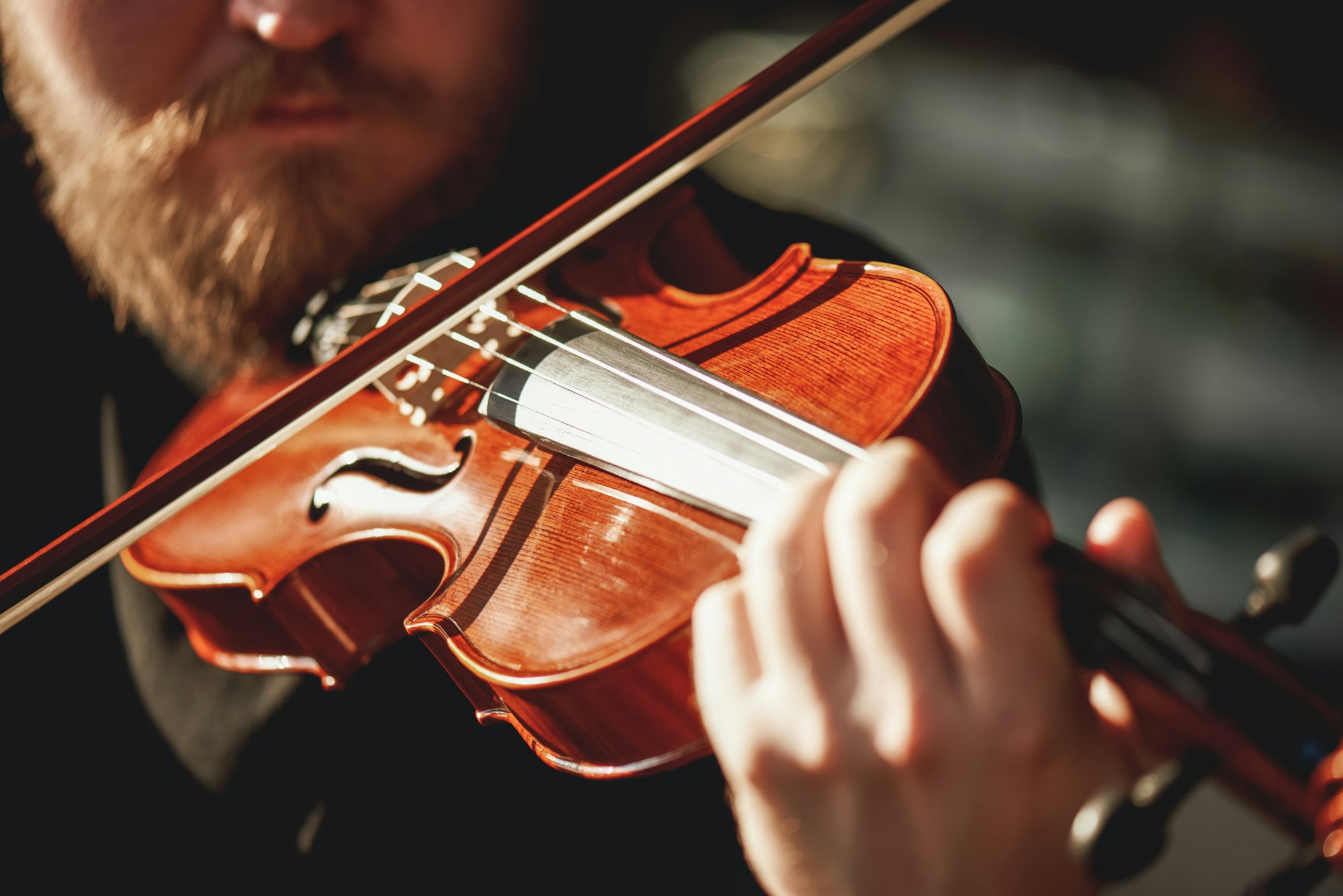 Playing classical music. Close up view of beard violinist playing classical music on the brown wood
