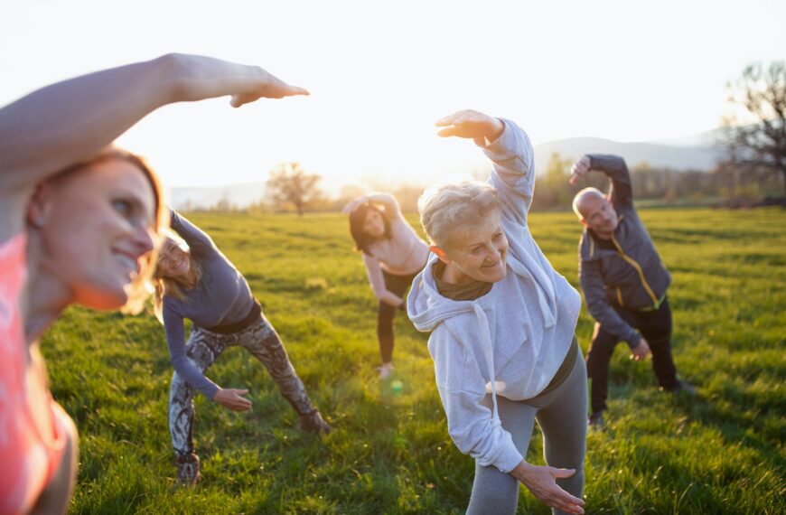 Seniors with sport instructor doing exercise outdoors in nature at sunset, active lifestyle.