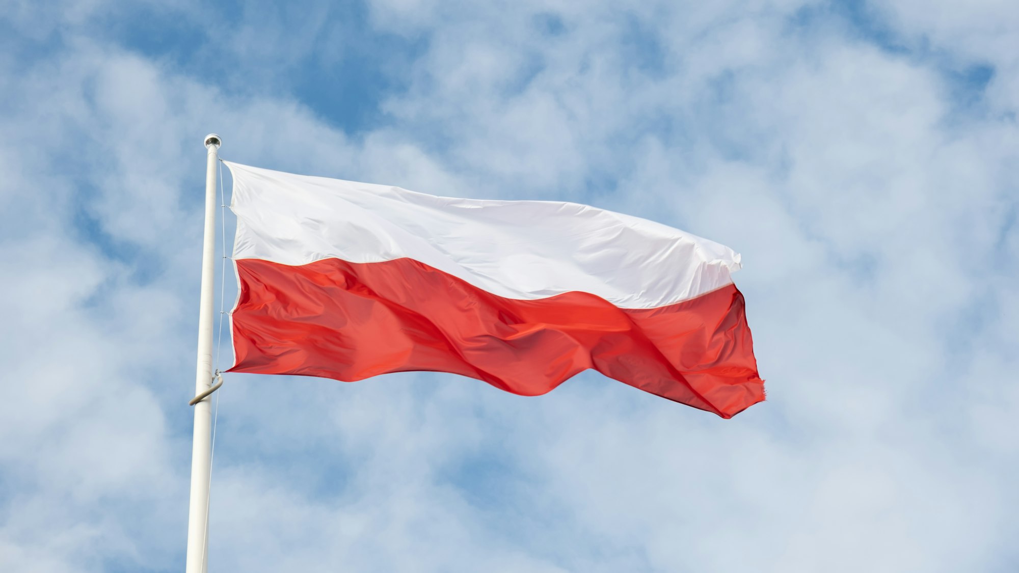 Flag of Poland waving at wind against beautiful blue sky. Polish flag White and red flutters on blue