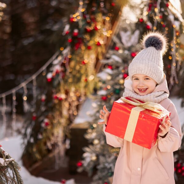 Little girl with a Christmas gift outdoors in winter on Christmas Eve.