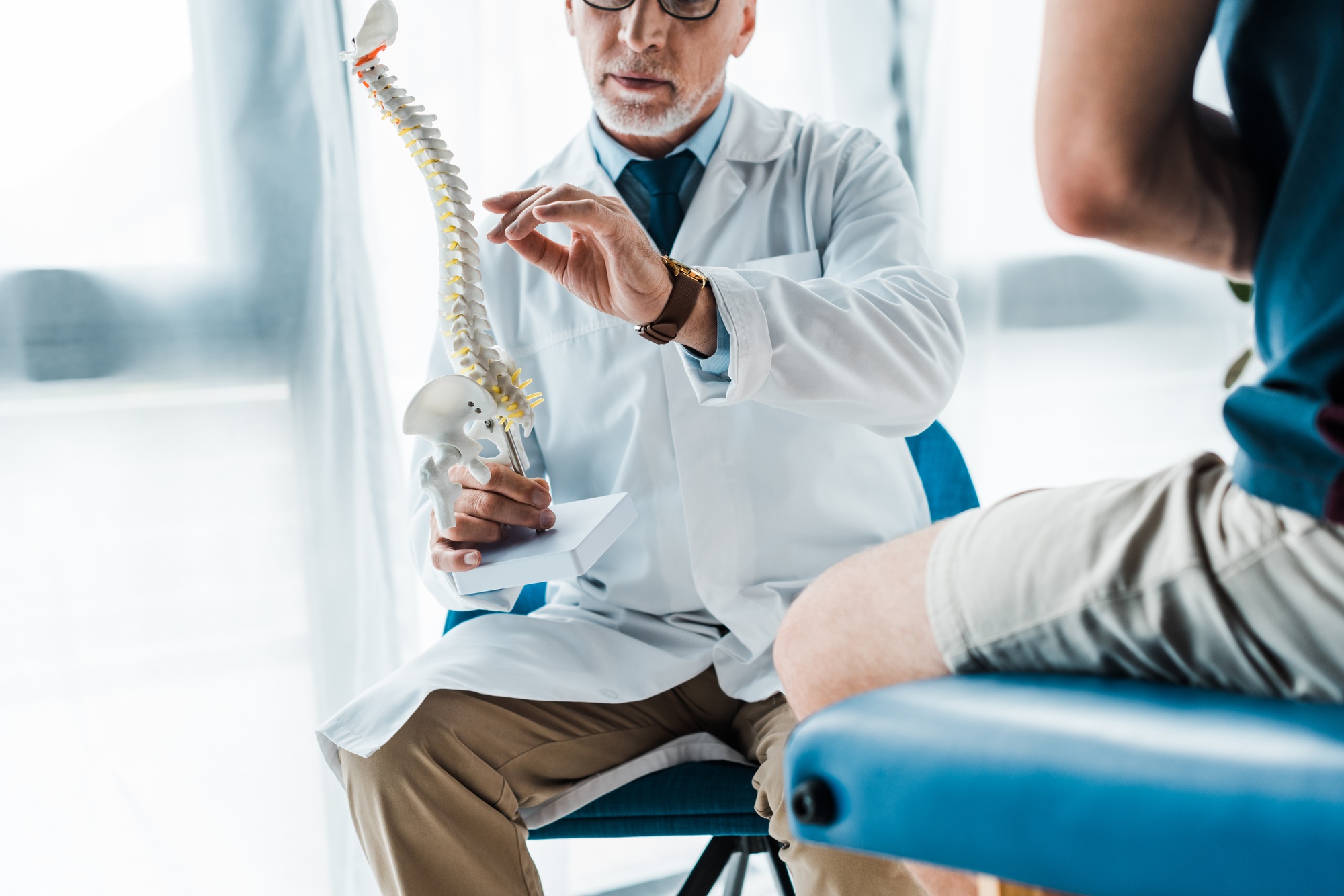cropped view of man sitting near doctor gesturing while holding spine model