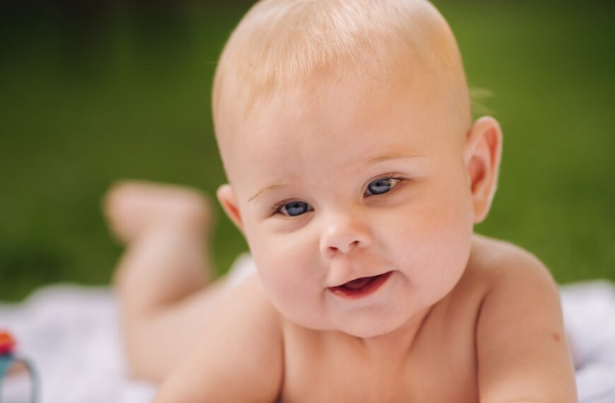 Cute happy toddler lying on a blanket on the grass outdoors in summer