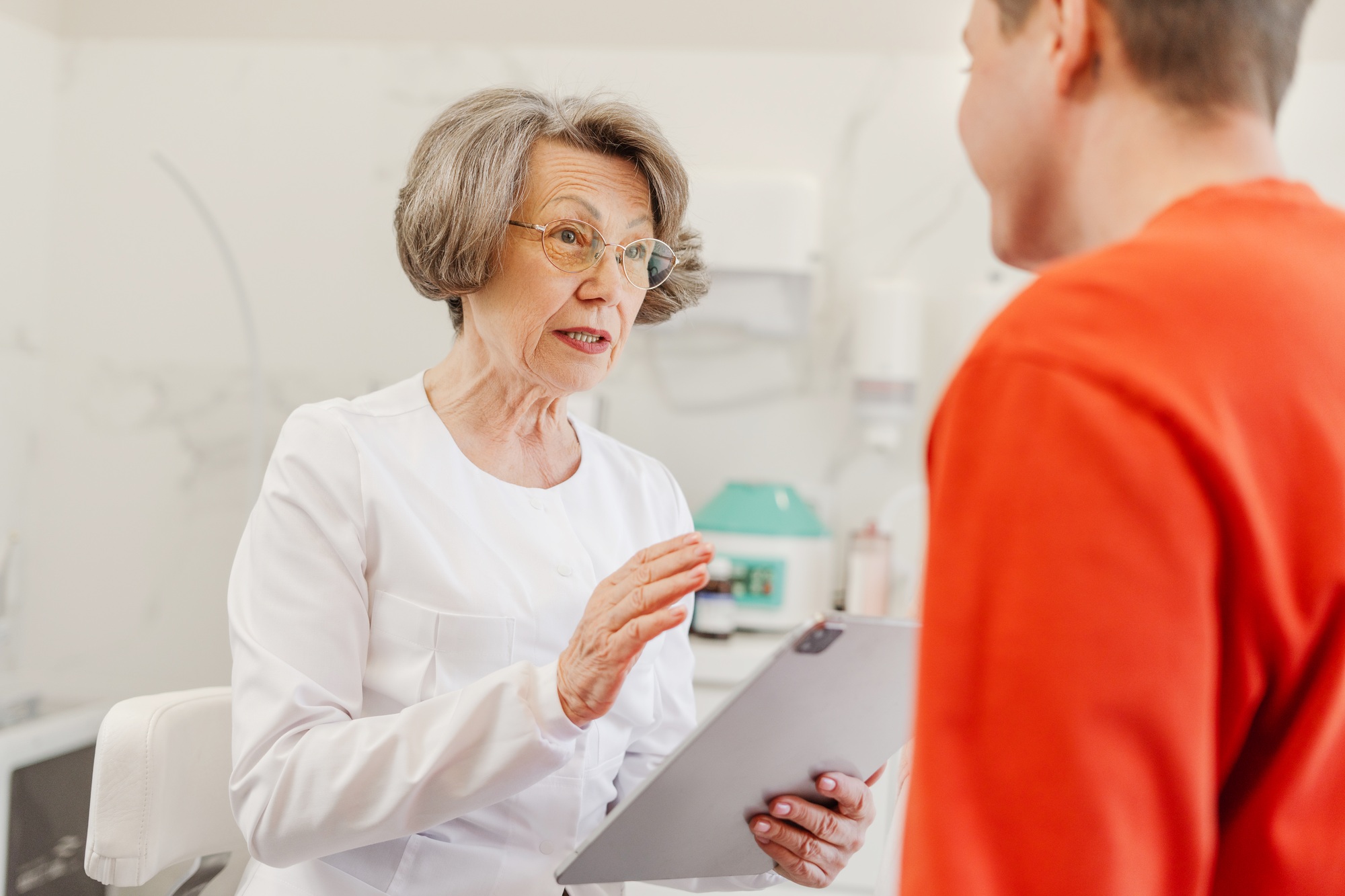 Attractive, senior, mature female cosmetologist communicates with patient, asking about health
