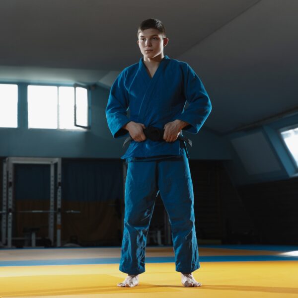 Young judo fighter in kimono posing comfident in the gym, strong and healthy