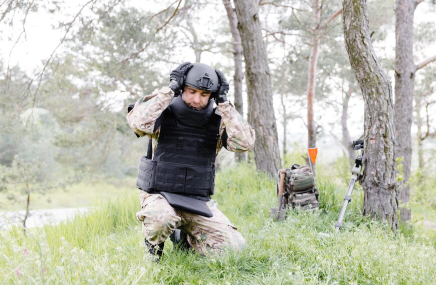A man in a military uniform and a bulletproof vest works in the forest to demine the territory