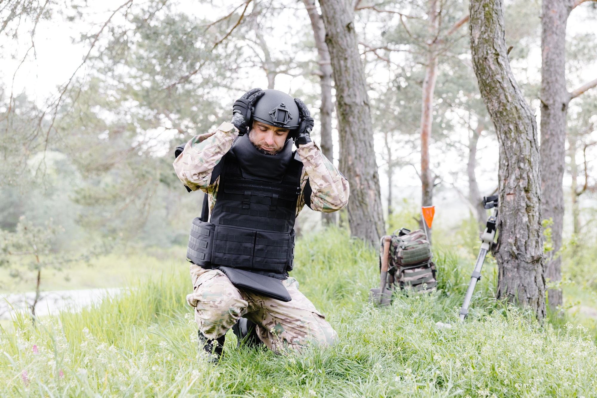 A man in a military uniform and a bulletproof vest works in the forest to demine the territory