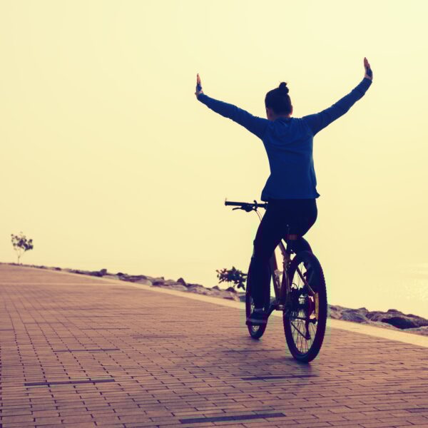 free woman cyclist outstretched arms on sunrise seaside