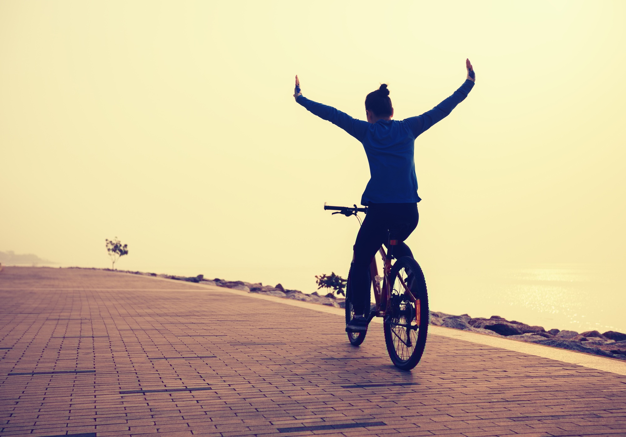 free woman cyclist outstretched arms on sunrise seaside