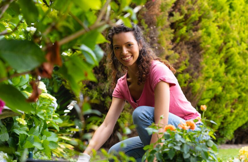 Portrait of smiling young biracial woman crouching while gardening in backyard
